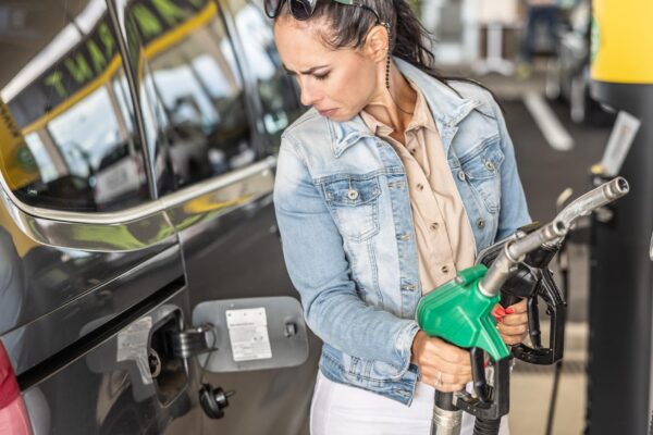 Woman holding gas and diesel pistols in the service station looks at the open gas tank of her car