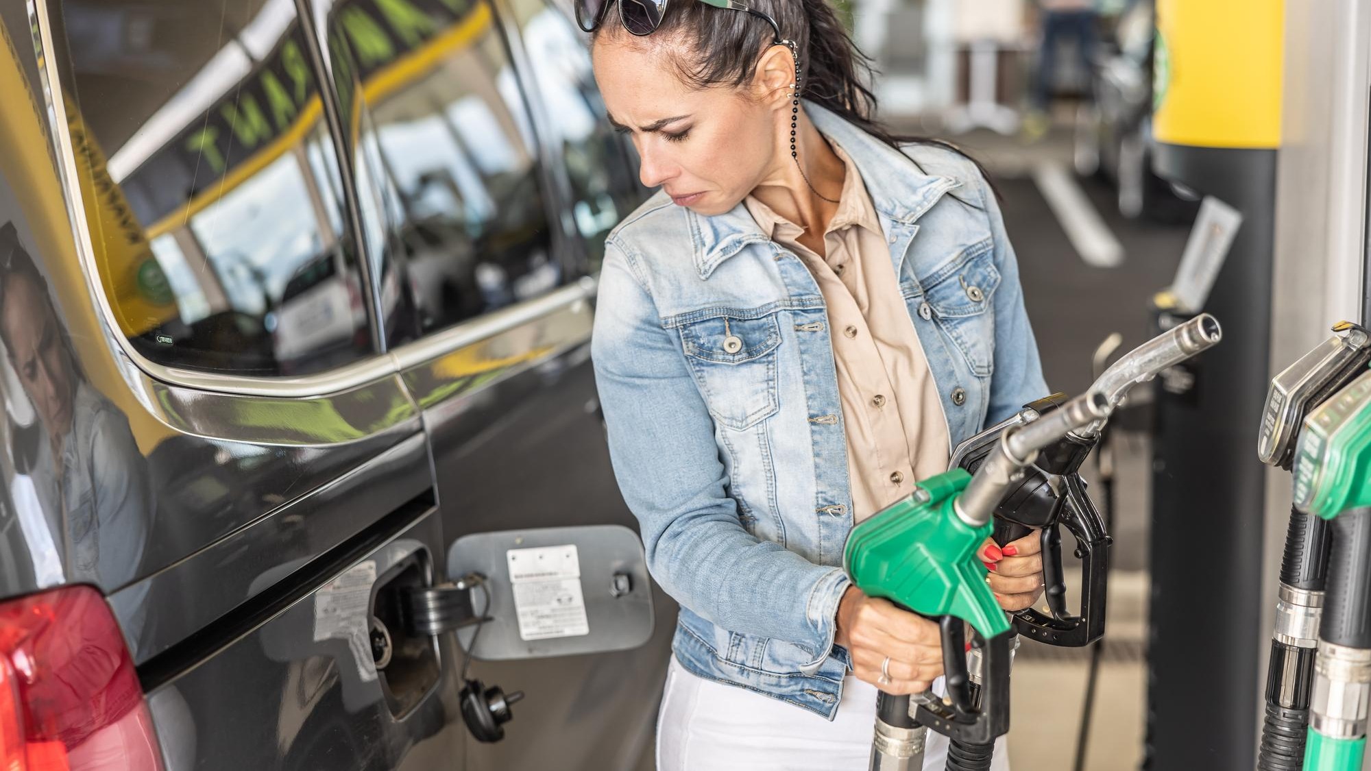 Woman holding gas and diesel pistols in the service station looks at the open gas tank of her car
