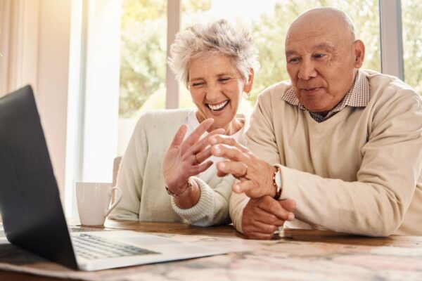 Laptop video call and senior couple wave talking to contact and laughing in home Comic technology and smile of happy retired man and woman with computer for virtual chat or online communication