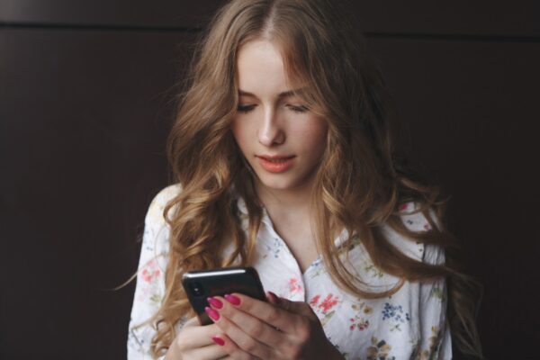 Picture of young cute blonde girl with a cup of coffee holding phone and typing text beautiful yong woman with bright pink nails