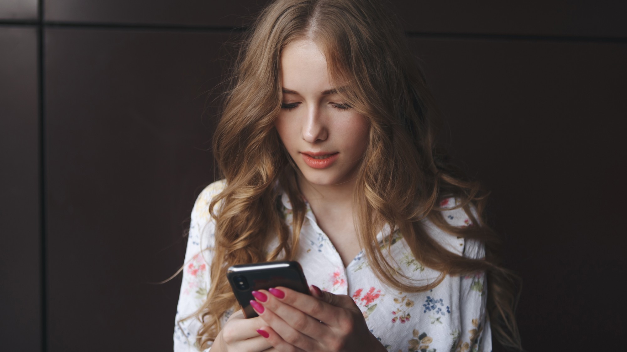 Picture of young cute blonde girl with a cup of coffee holding phone and typing text beautiful yong woman with bright pink nails
