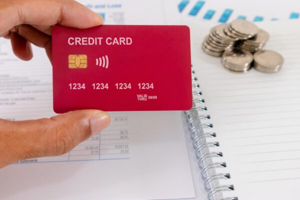 Hand holding a credit card on his desk with paperwork blank notebook and coins