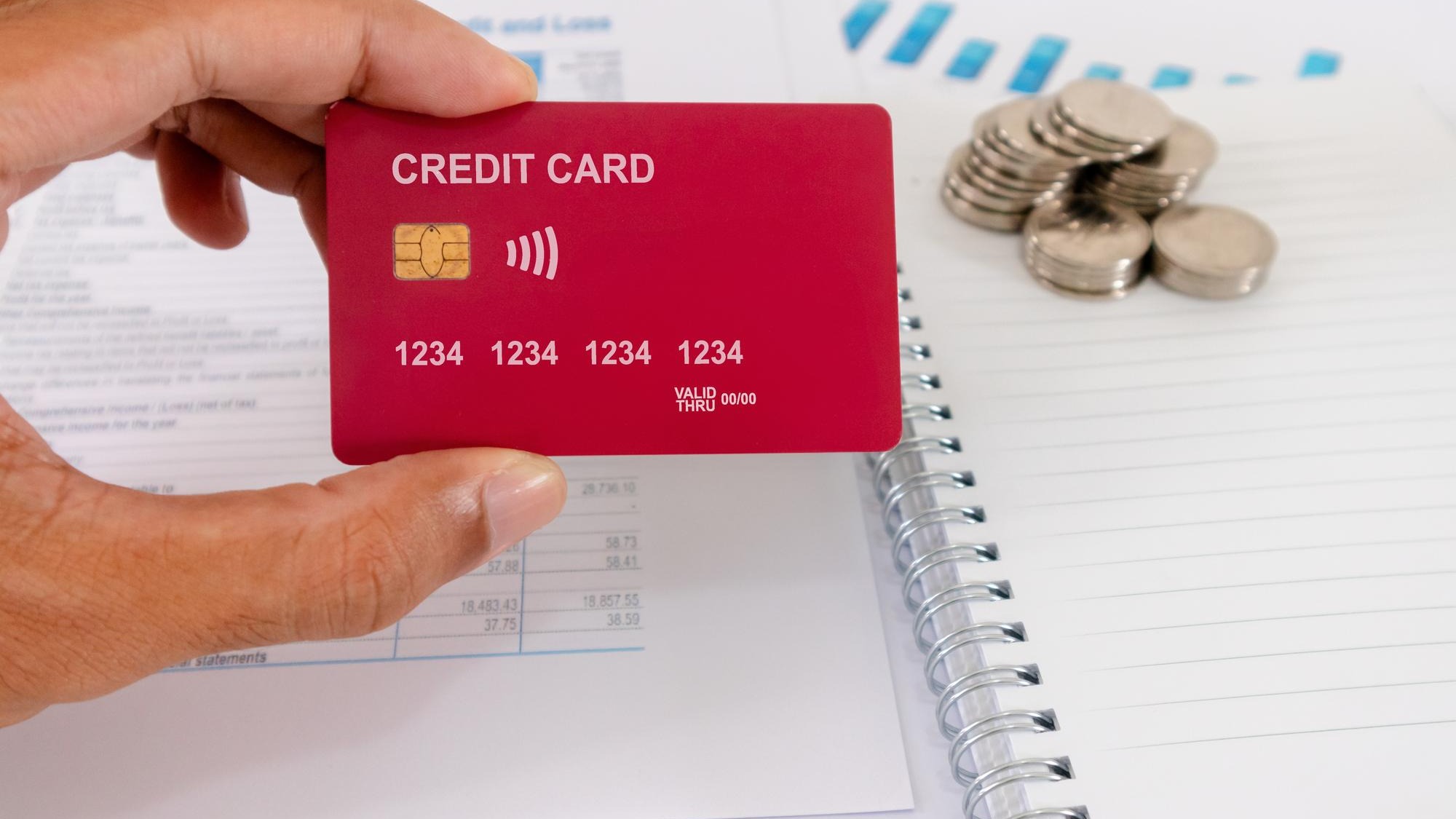 Hand holding a credit card on his desk with paperwork blank notebook and coins