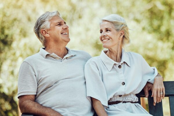 Love retirement and couple on bench in park with smile relax and bonding time in nature together Romance senior man and retired woman sitting in garden happy people and romantic summer weekend