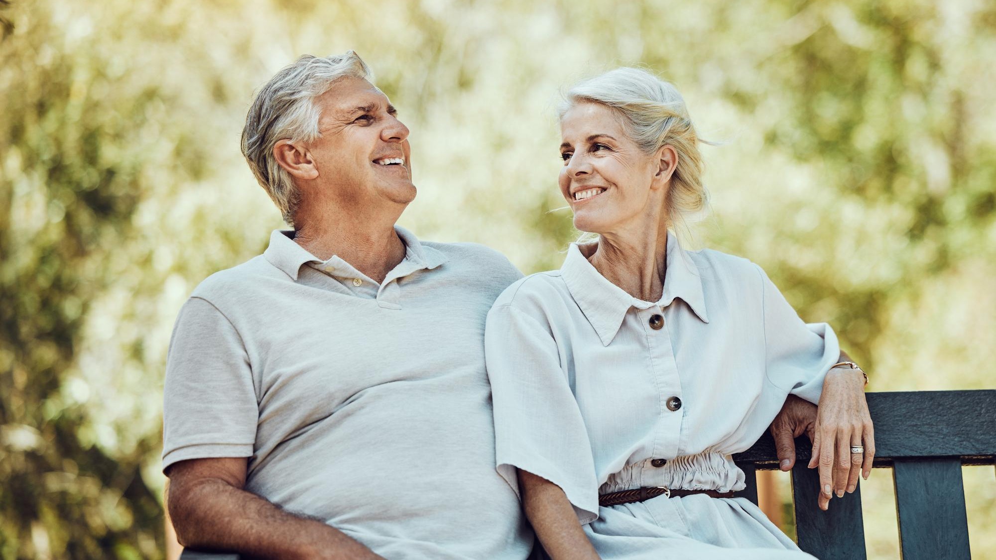 Love retirement and couple on bench in park with smile relax and bonding time in nature together Romance senior man and retired woman sitting in garden happy people and romantic summer weekend