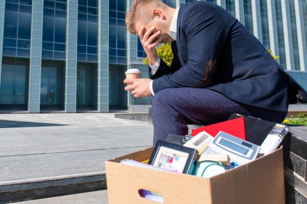 Desperate man sitting at office building with his box next to him