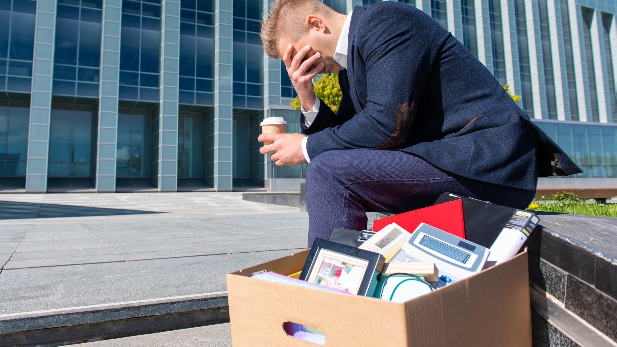 Desperate man sitting at office building with his box next to him