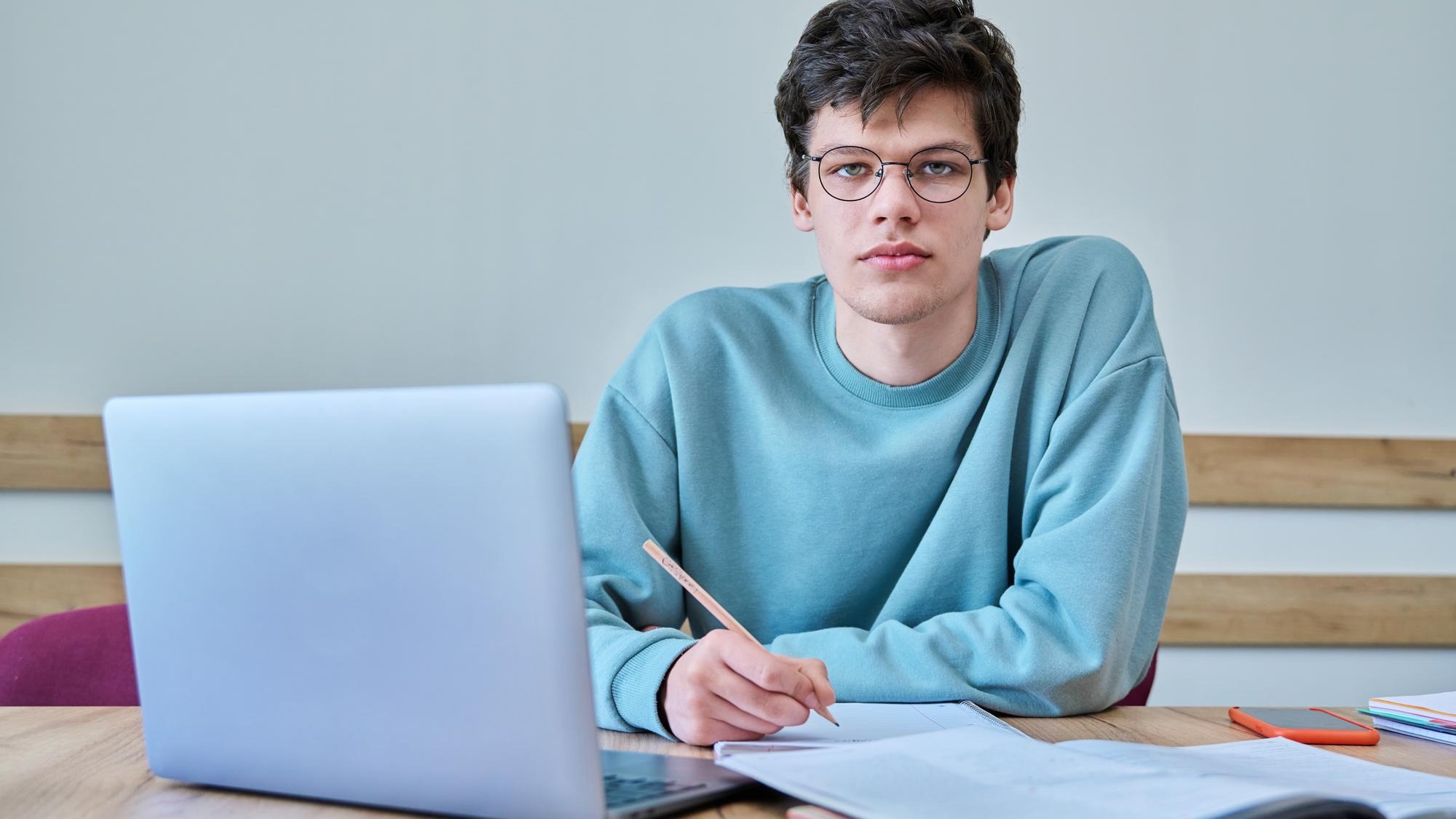 Young guy college student sitting at desk in classroom using laptop looking at camera