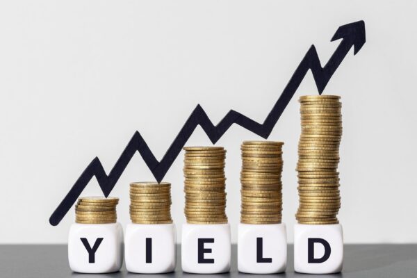 Stacks of coins with increasing chart arrow on top of a YIELD message on cube blocks Copy space