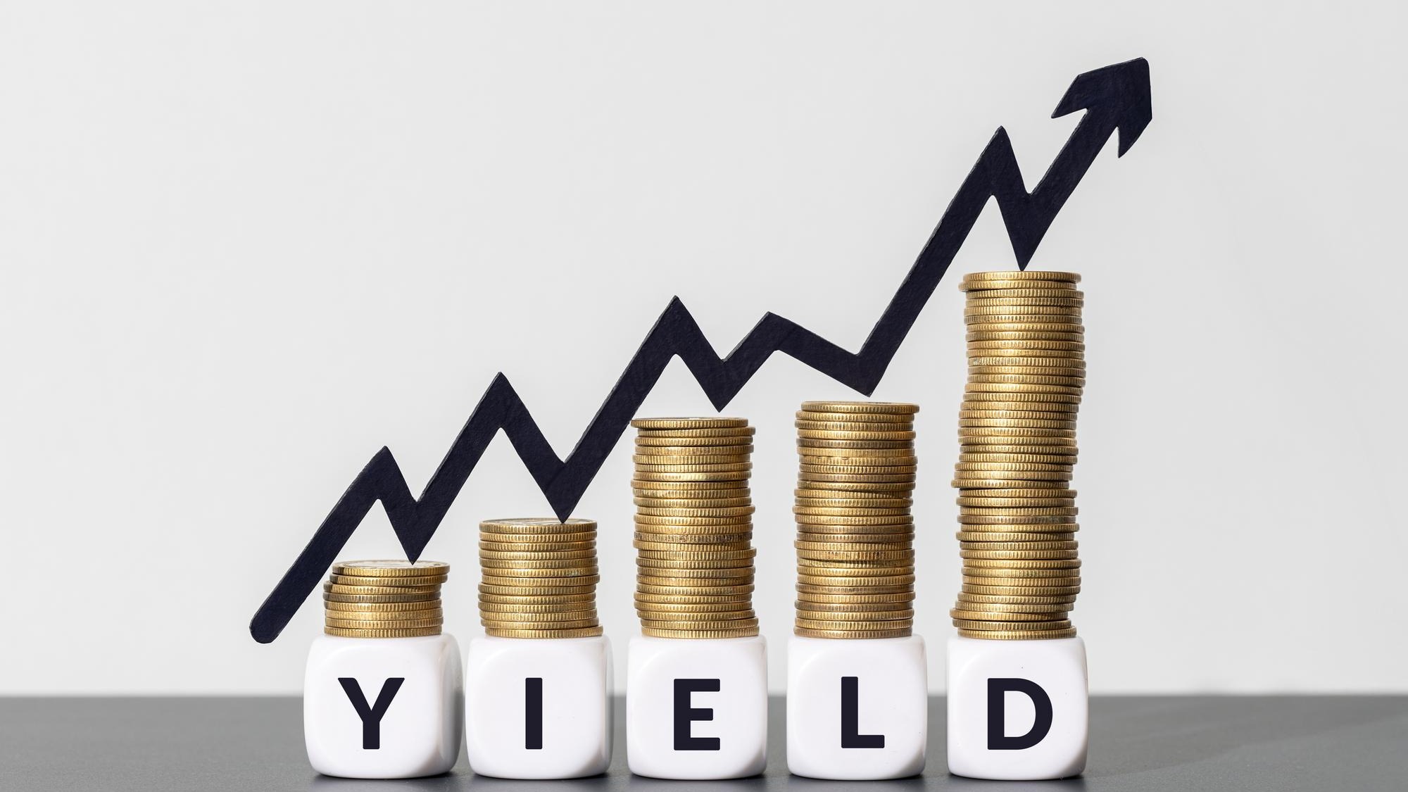 Stacks of coins with increasing chart arrow on top of a YIELD message on cube blocks Copy space