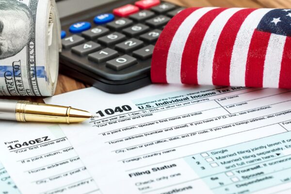 Tax forms with small american flag calculator nad roll of dollar bills on the table Business concept