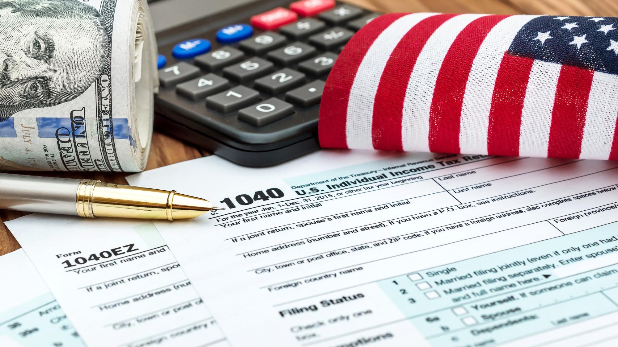 Tax forms with small american flag calculator nad roll of dollar bills on the table Business concept
