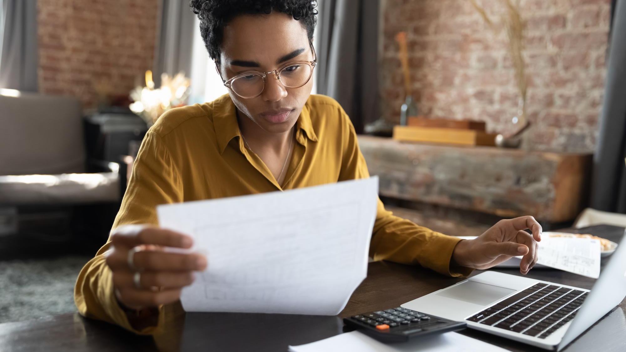 Focused young African American woman in eyeglasses looking through paper documents managing business affairs summarizing taxes planning future investments accounting alone at home office