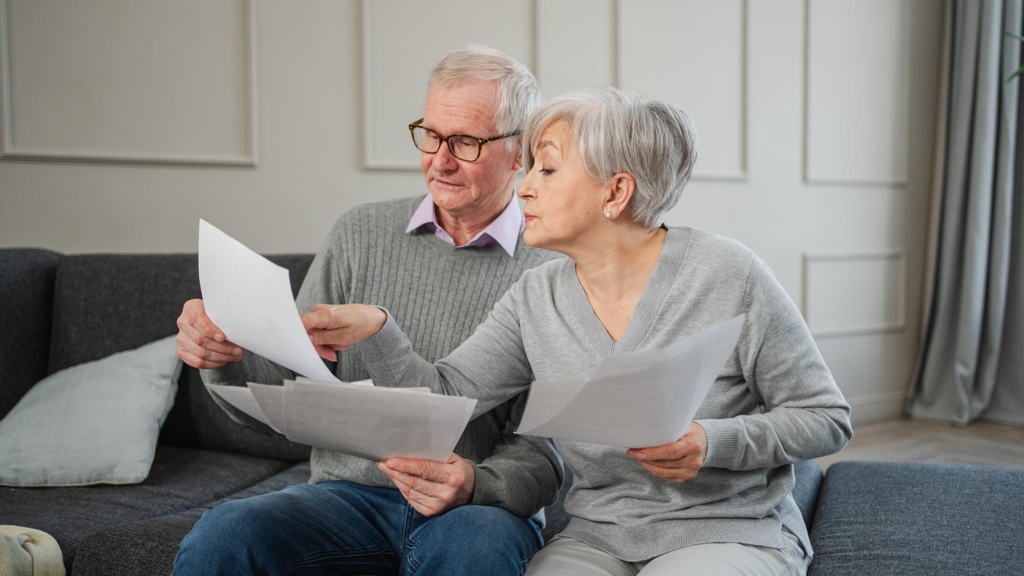 Sad tired disappointed middle aged senior couple sit with paper document unhappy older mature man