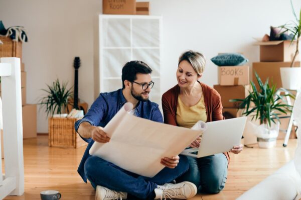 Happy couple examining blueprints and using laptop at their new apartment
