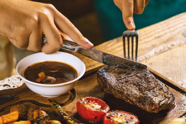 Woman cutting grilled beef steak served on wooden board with vegetables