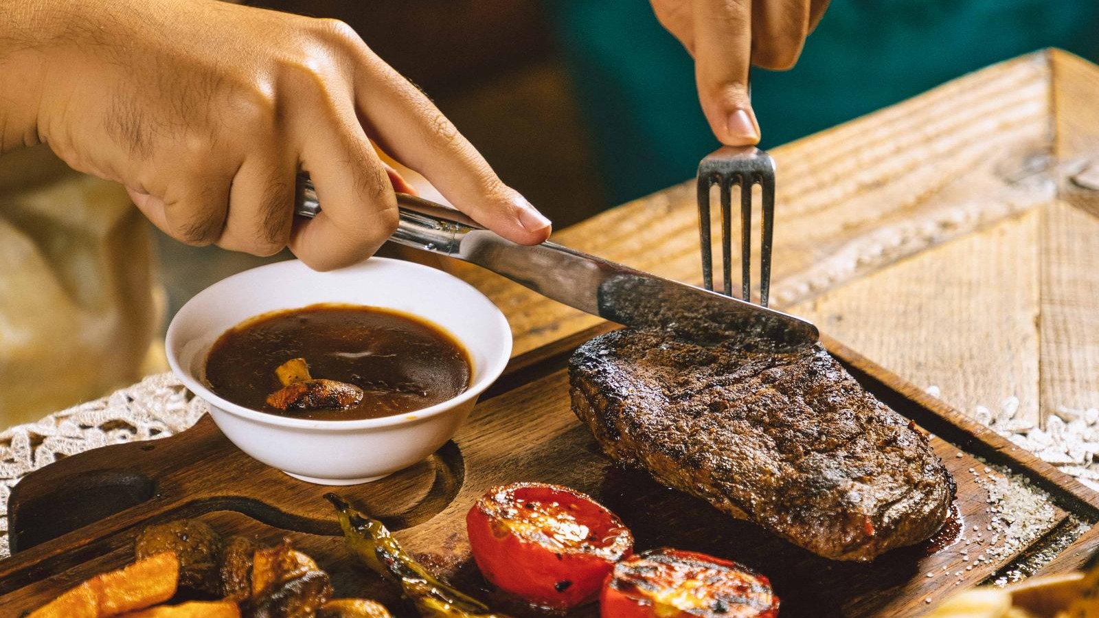 Woman cutting grilled beef steak served on wooden board with vegetables