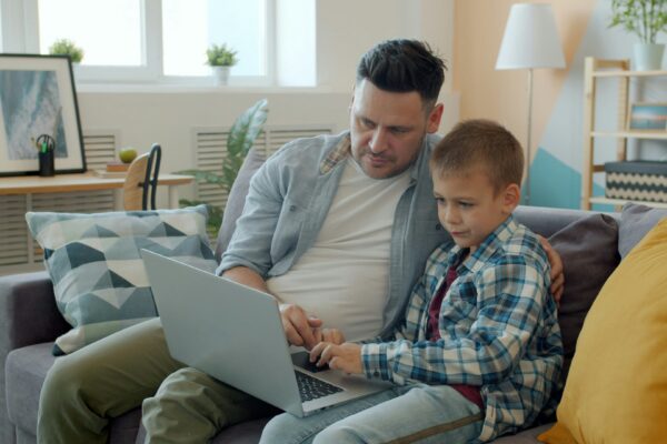 Father and son using a laptop on the couch.