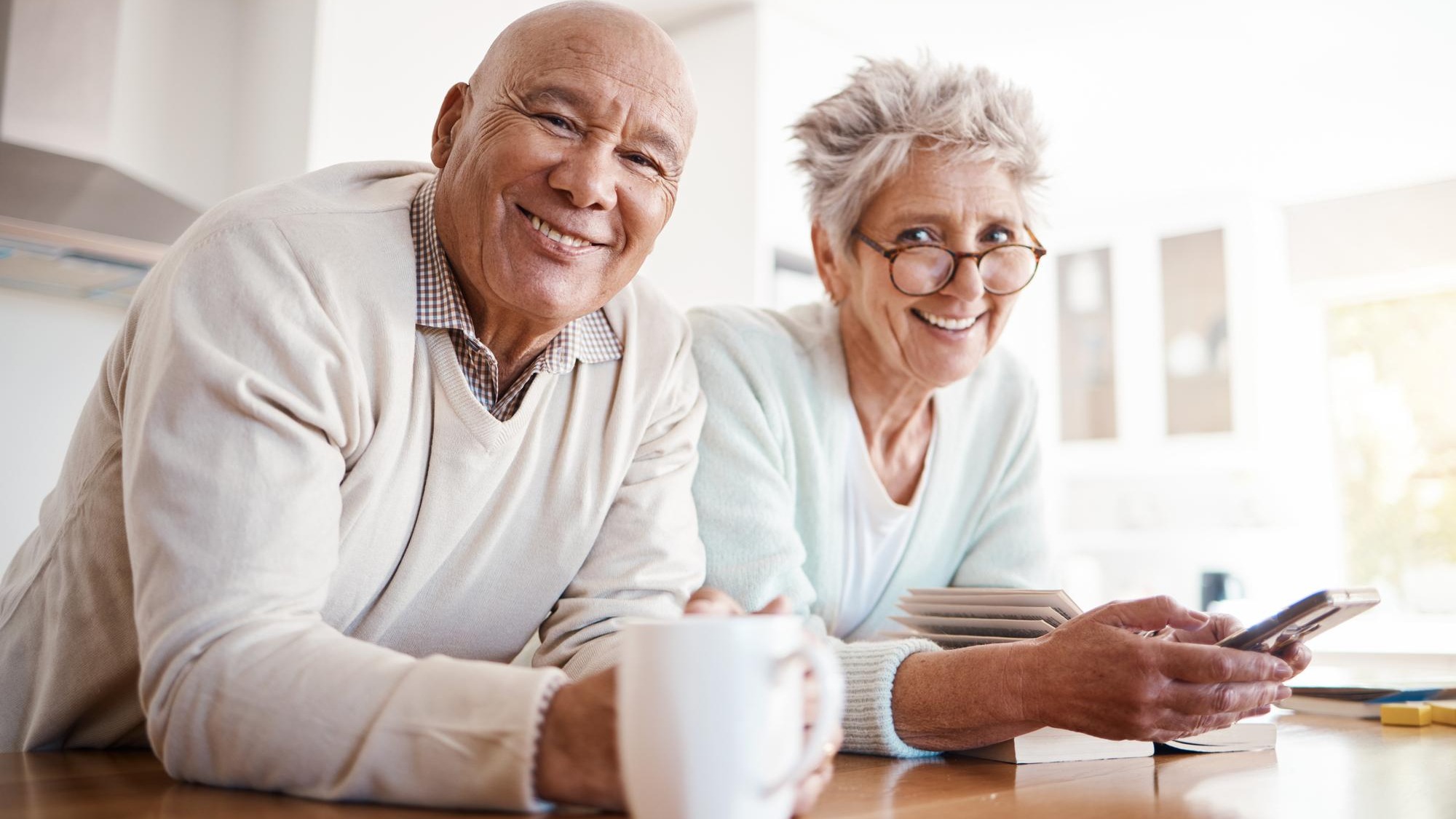 Portrait senior and old interracial couple relax in home kitchen in the morning with coffee happy smile and confident together Old man and elderly woman on counter enjoying retirement in happiness