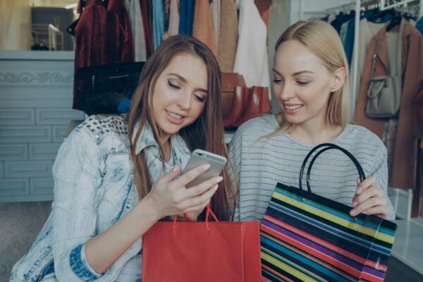 Two friends look at a phone after shopping.