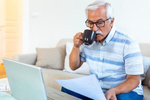 Focused greyhaired elderly man sit on couch reading bank notifications calculating domestic expenditures concentrated modern mature male consider financial paperwork pay bills on laptop online
