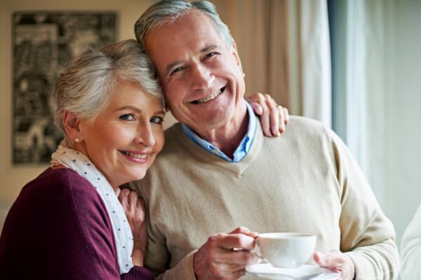 Senior couple tea and window in home for relax love and portrait for married man and woman Living room house and calm for retired people coffee or beverage for romance and peace in Germany