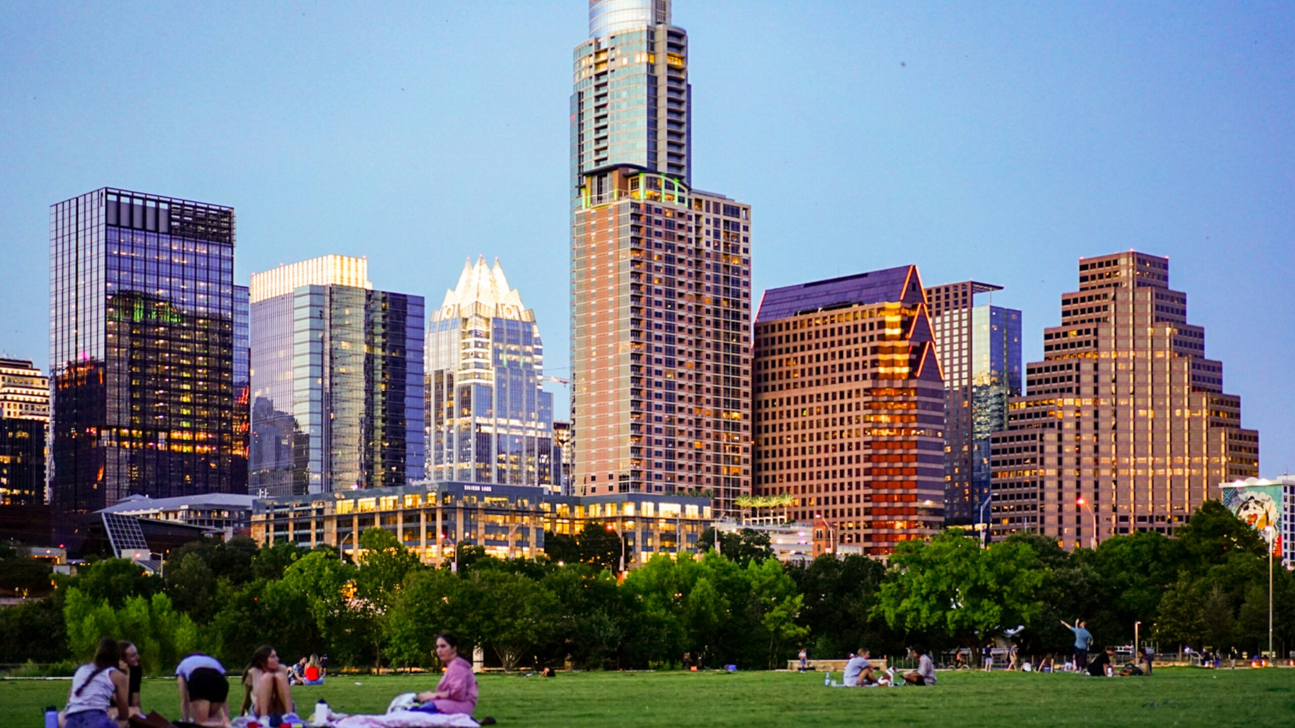 people sitting on green grass field near city buildings during daytime