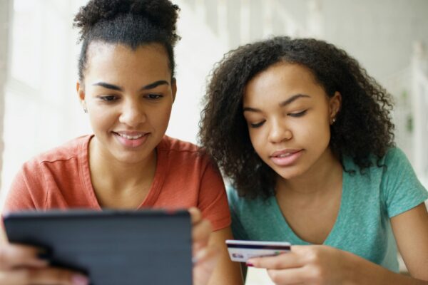 Two young women looking at a tablet with credit card.