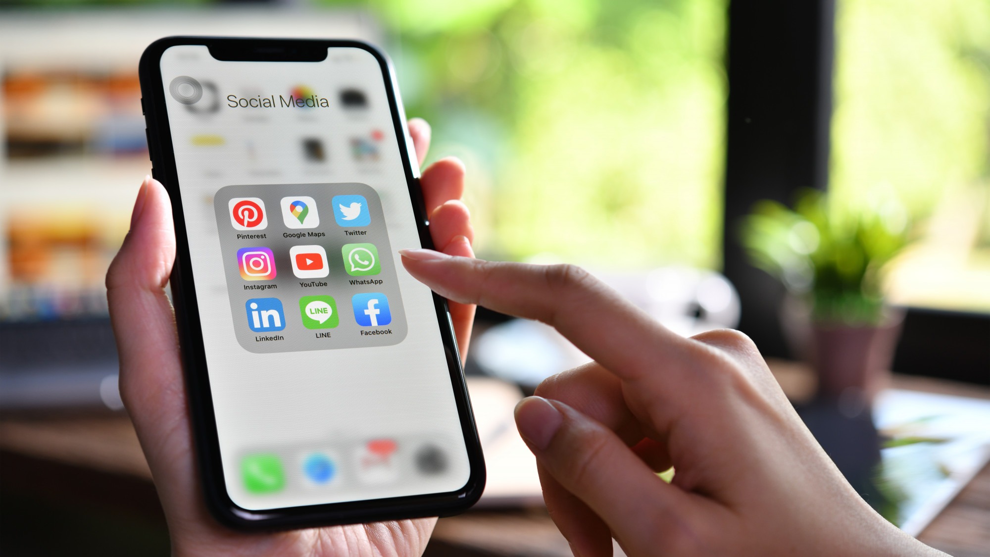 Female holding a smartphone with icons of social media on the screen at the coffee shop.