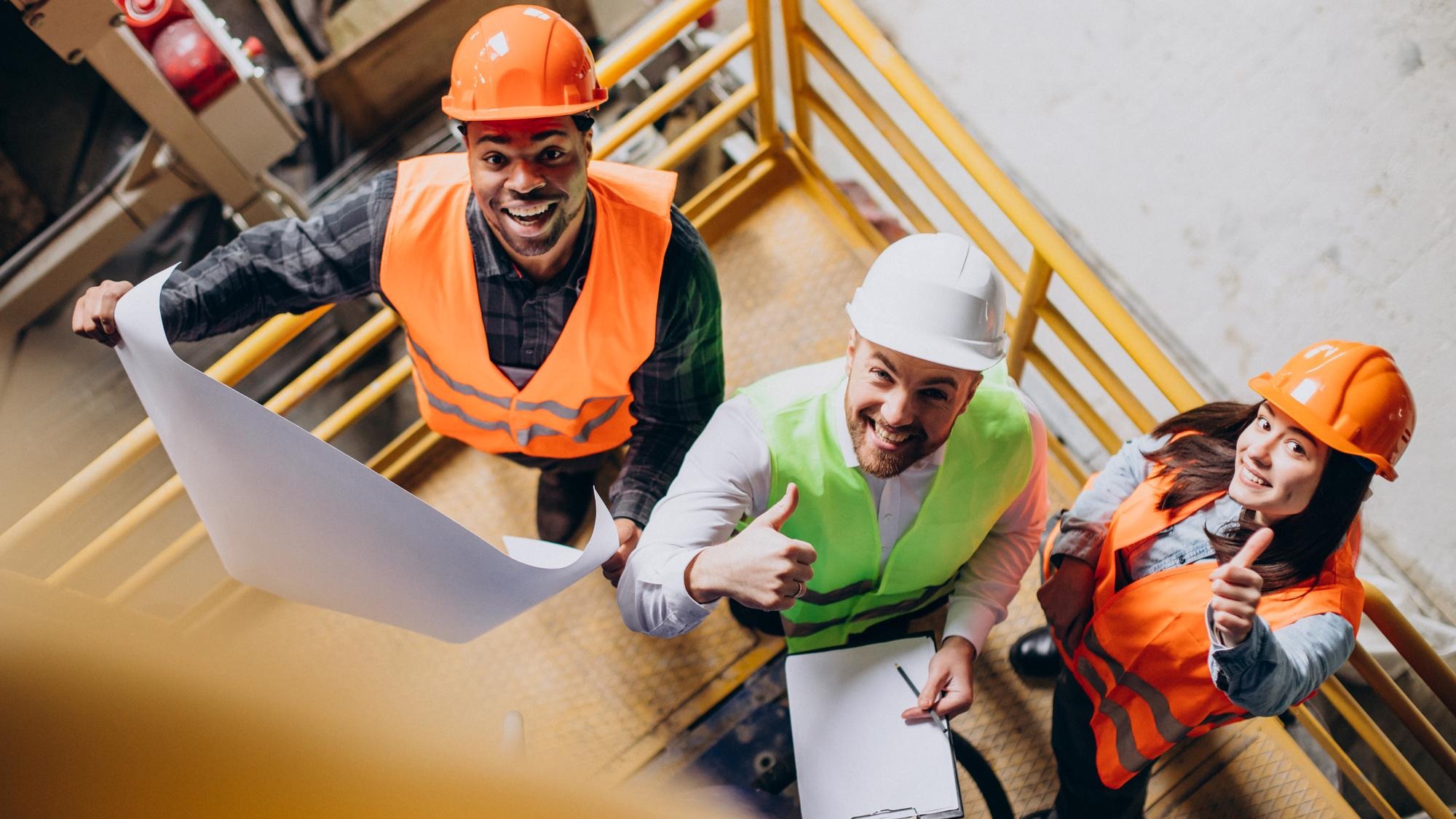 Three factory workers in safety hats discussing manufacture plan