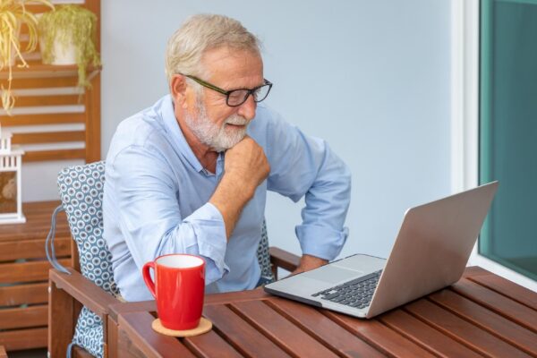 Senior man executive with white hair using computer laptop watching movie at home with coffee
