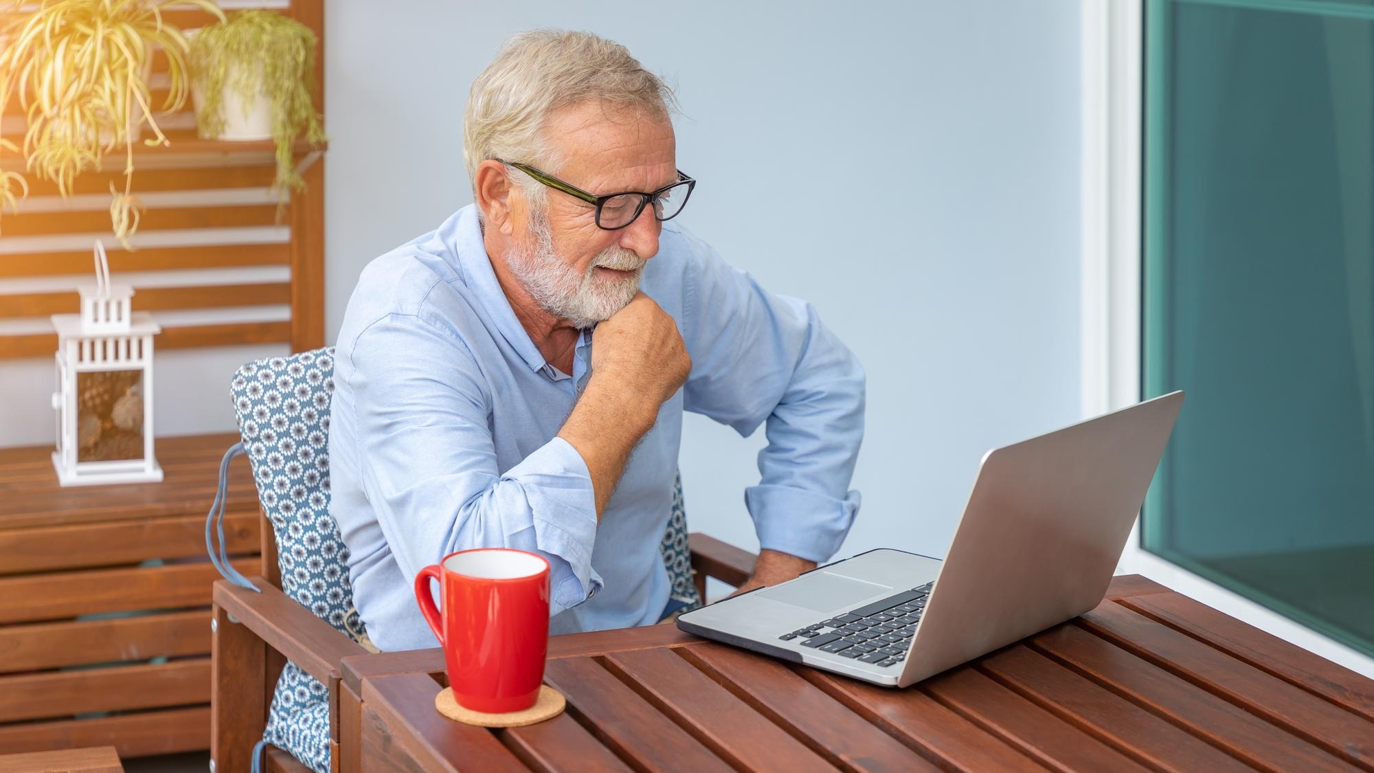 Senior man executive with white hair using computer laptop watching movie at home with coffee