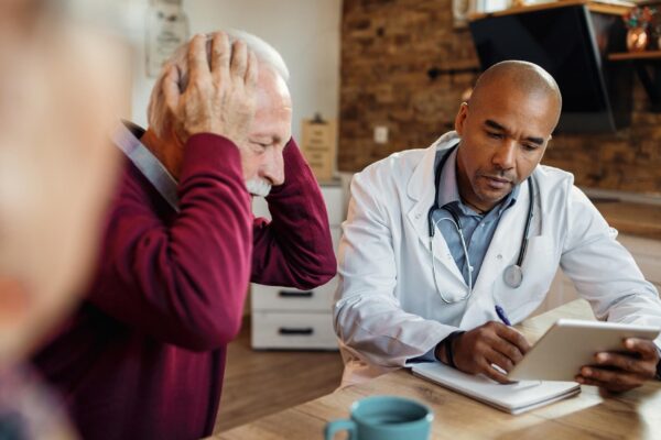 Black doctor using touchpad and taking notes during a visit at senior man's home