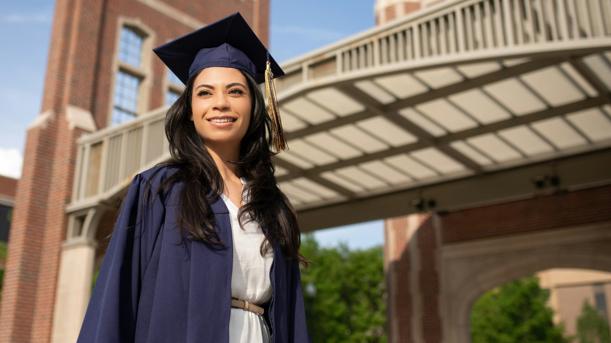 a woman in a cap and gown standing in front of a bridge