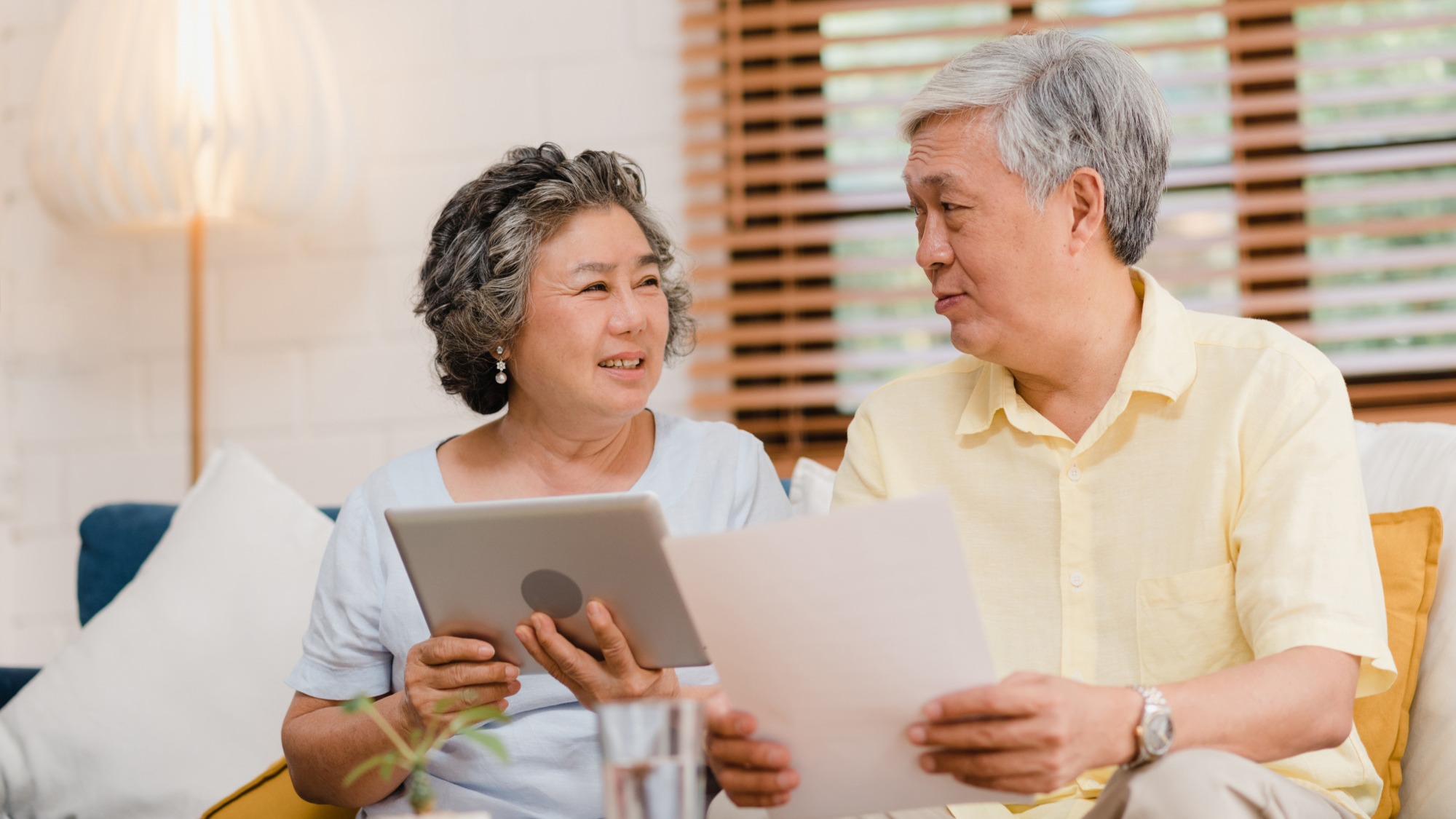 Asian elderly couple using tablet watching TV in living room at home, couple enjoy love moment while lying on sofa when relaxed at home.