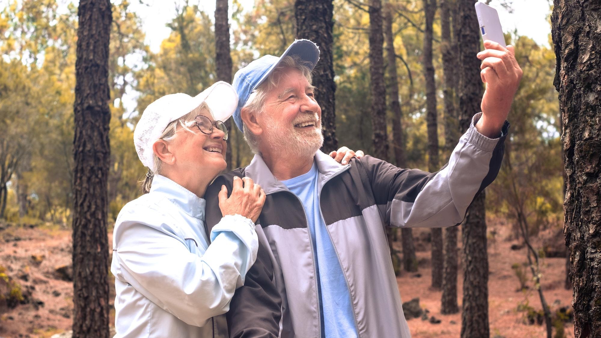 Video call concept Happy bonding senior couple enjoying mountain hike in the forest expressing joy