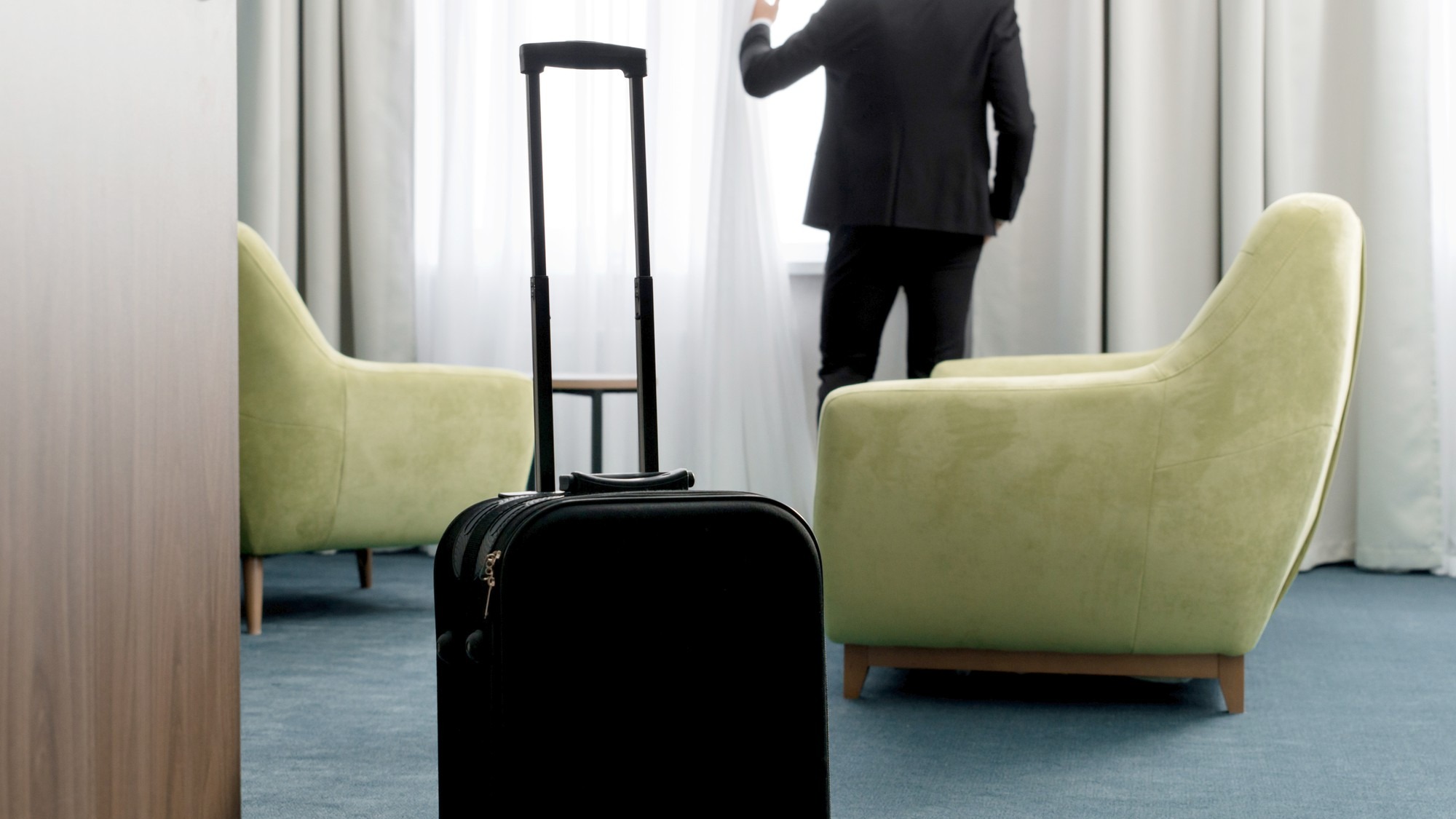 Rear view of businessman wearing dark suit standing in hotel room looking into window