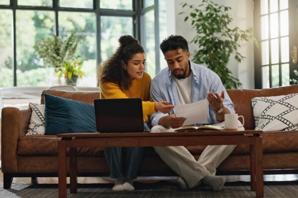 Home couple and discussion with paperwork financial analysis and checking info with laptop or app Asset management online and people with documents in living room bills and planning in house