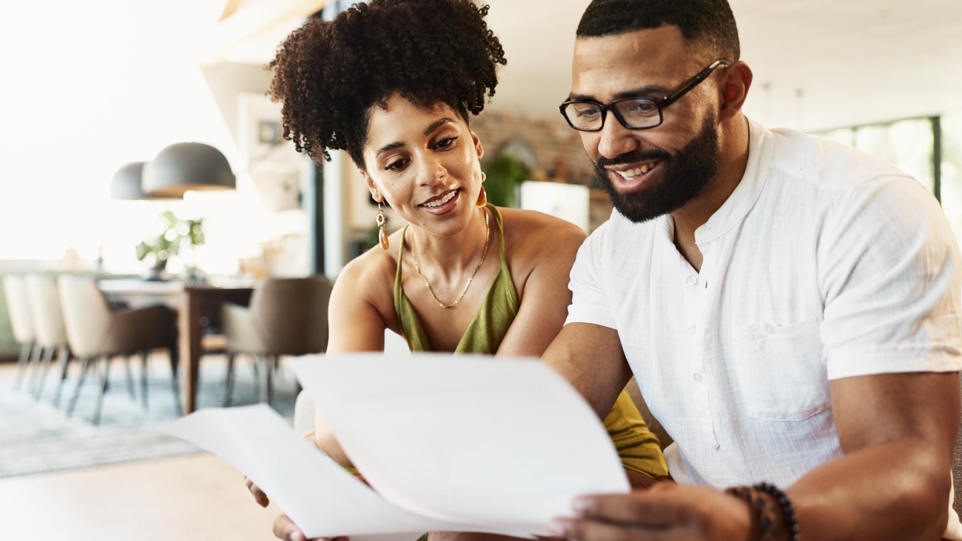 Couple paperwork and couch in home with investment budgeting and financial notes for saving Smile insurance and payment report with happy people together with documents for finance planning