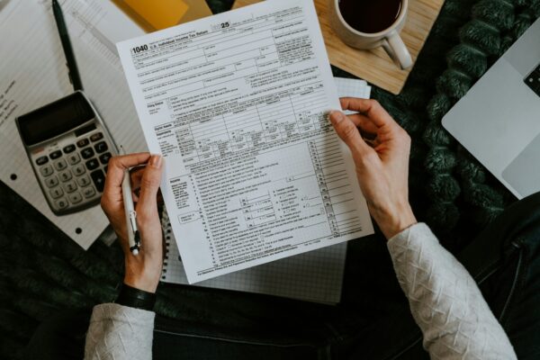 Hands holding tax forms with calculator and laptop.