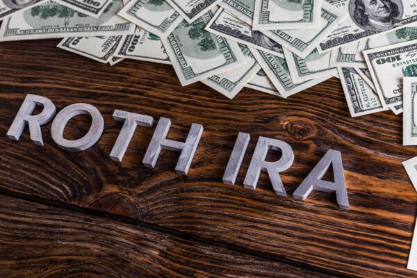 Words ROTH IRA laid on wooden surface with metal letters and us dollar banknotes