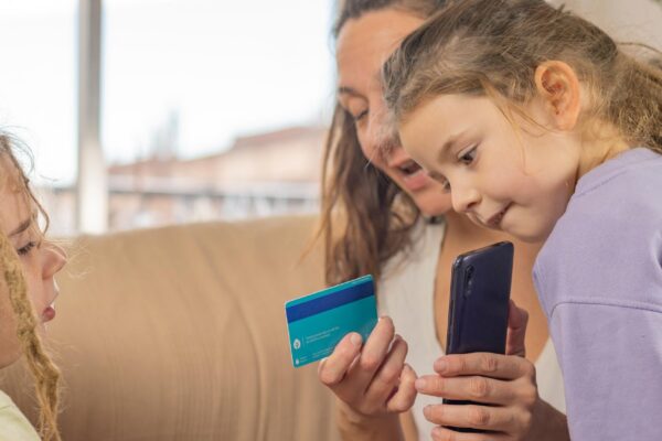 Mom with her bank card and smartphone shows young sons with dreadlocks how financial technology