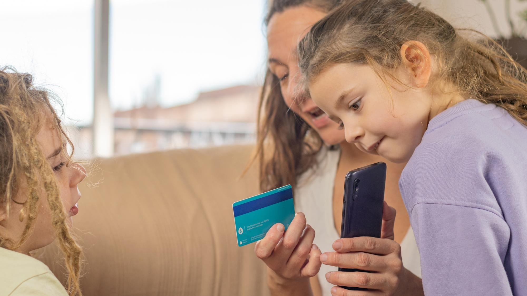 Mom with her bank card and smartphone shows young sons with dreadlocks how financial technology