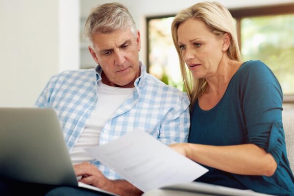 Couple couch and document with laptop and read finances or taxes for audit in living room Paperwork contract or online for mortgage investment investment or man with female person in home lounge