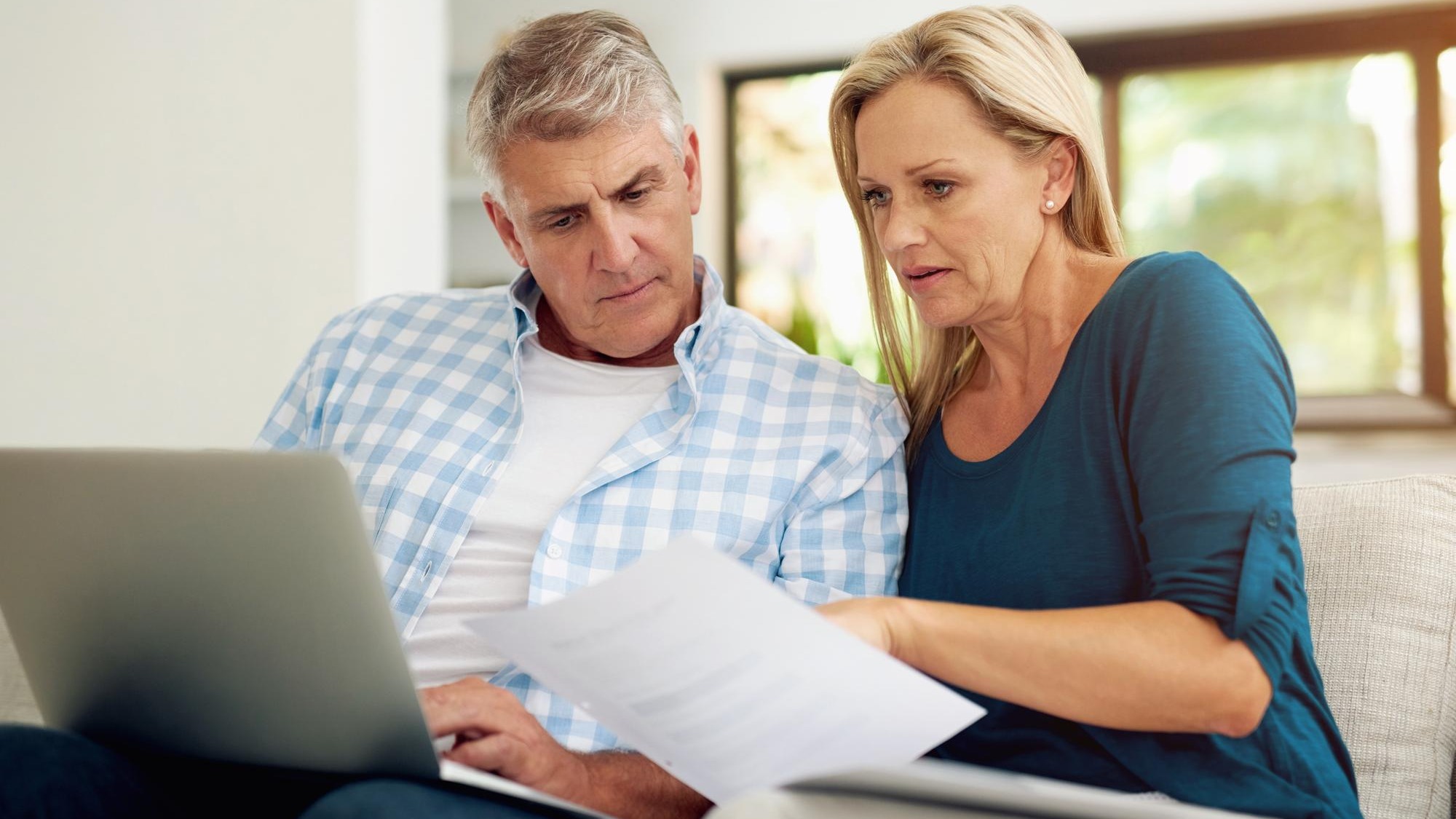 Couple couch and document with laptop and read finances or taxes for audit in living room Paperwork contract or online for mortgage investment investment or man with female person in home lounge