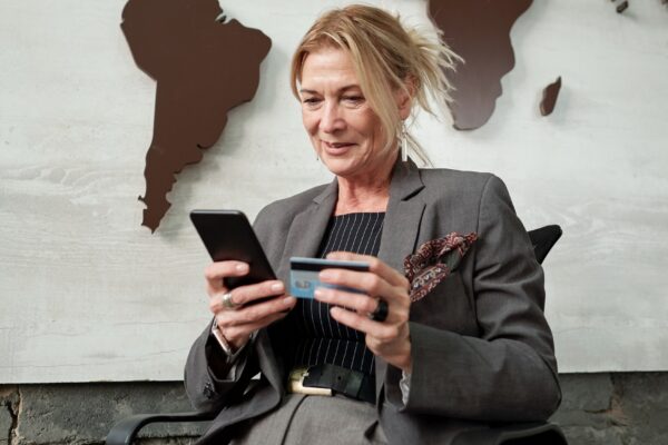 Content mature businesswoman sitting in chair and using smartphone and credit card while transferring money online