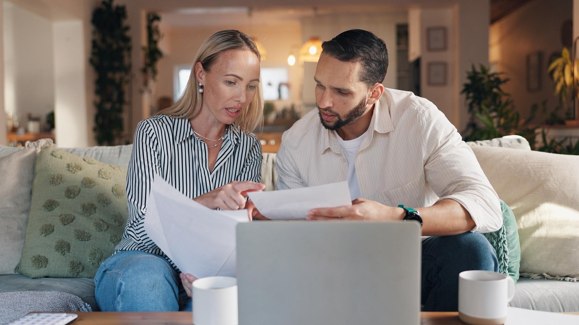 Home couple and laptop with talking for document financial bills and problem solving for budget Sofa woman and man with paperwork for tax deduction mortgage expenses or discussion in living room