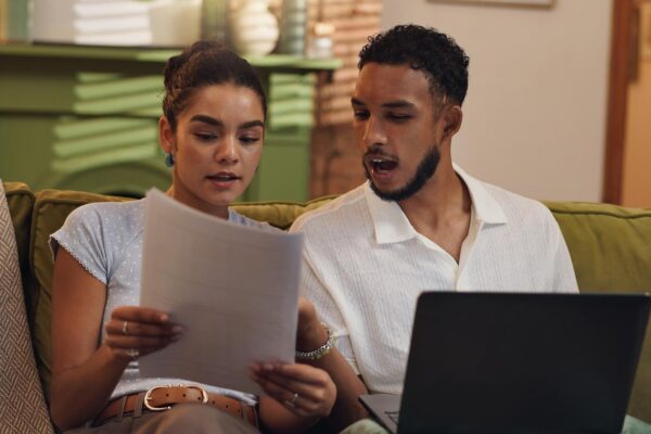 Couple finance and documents with laptop on sofa for budget planning expenses or bills at home Man woman or paperwork with computer for mortgage payment cost or financial invoices at house