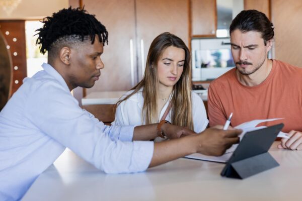 Diverse friends collaborating on project with tablet and documents at home