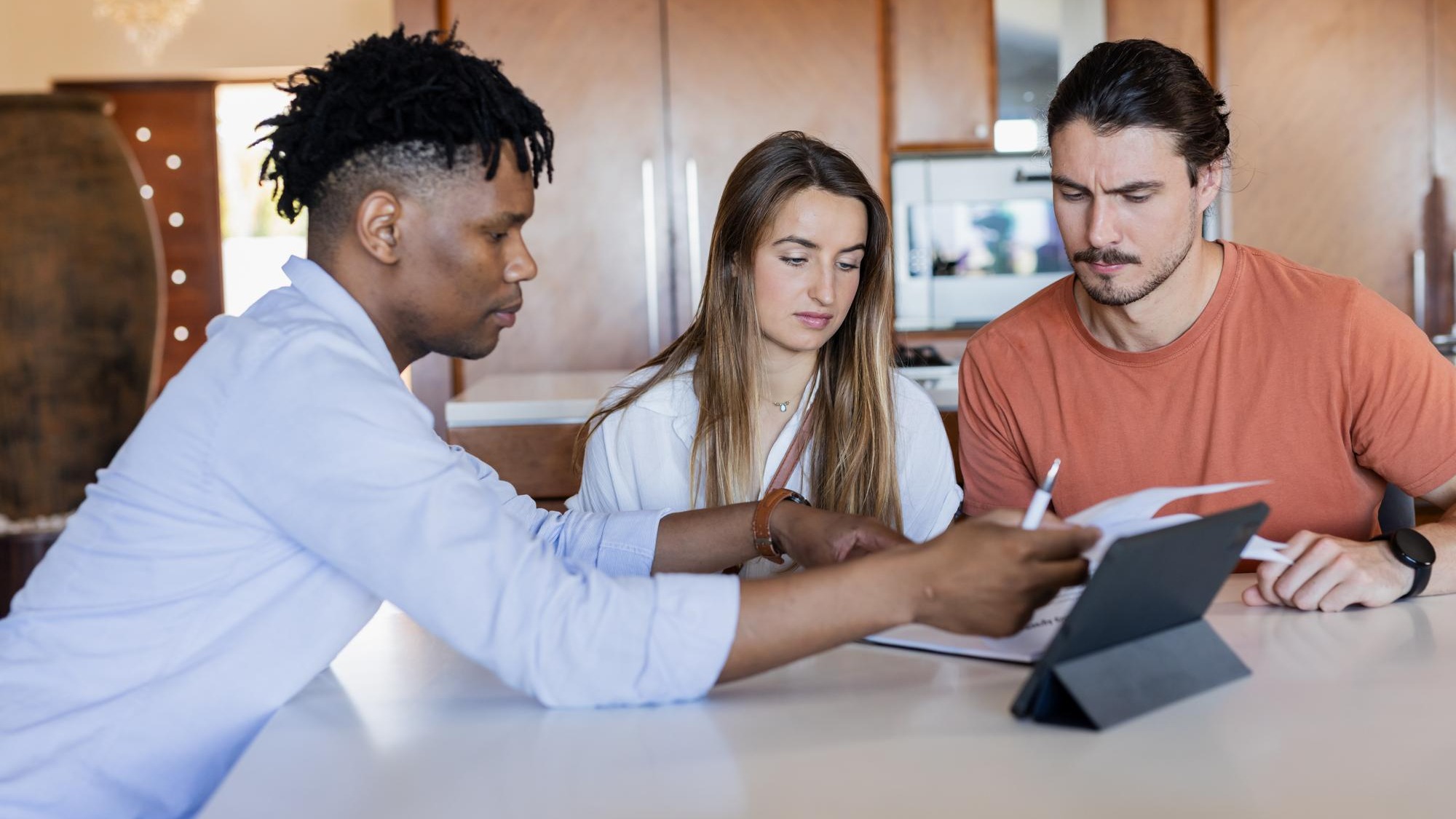 Diverse friends collaborating on project with tablet and documents at home